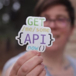 تعلم البرمجة 10 Close-up of a person holding a colorful API-themed sticker with trees blurred in the background.